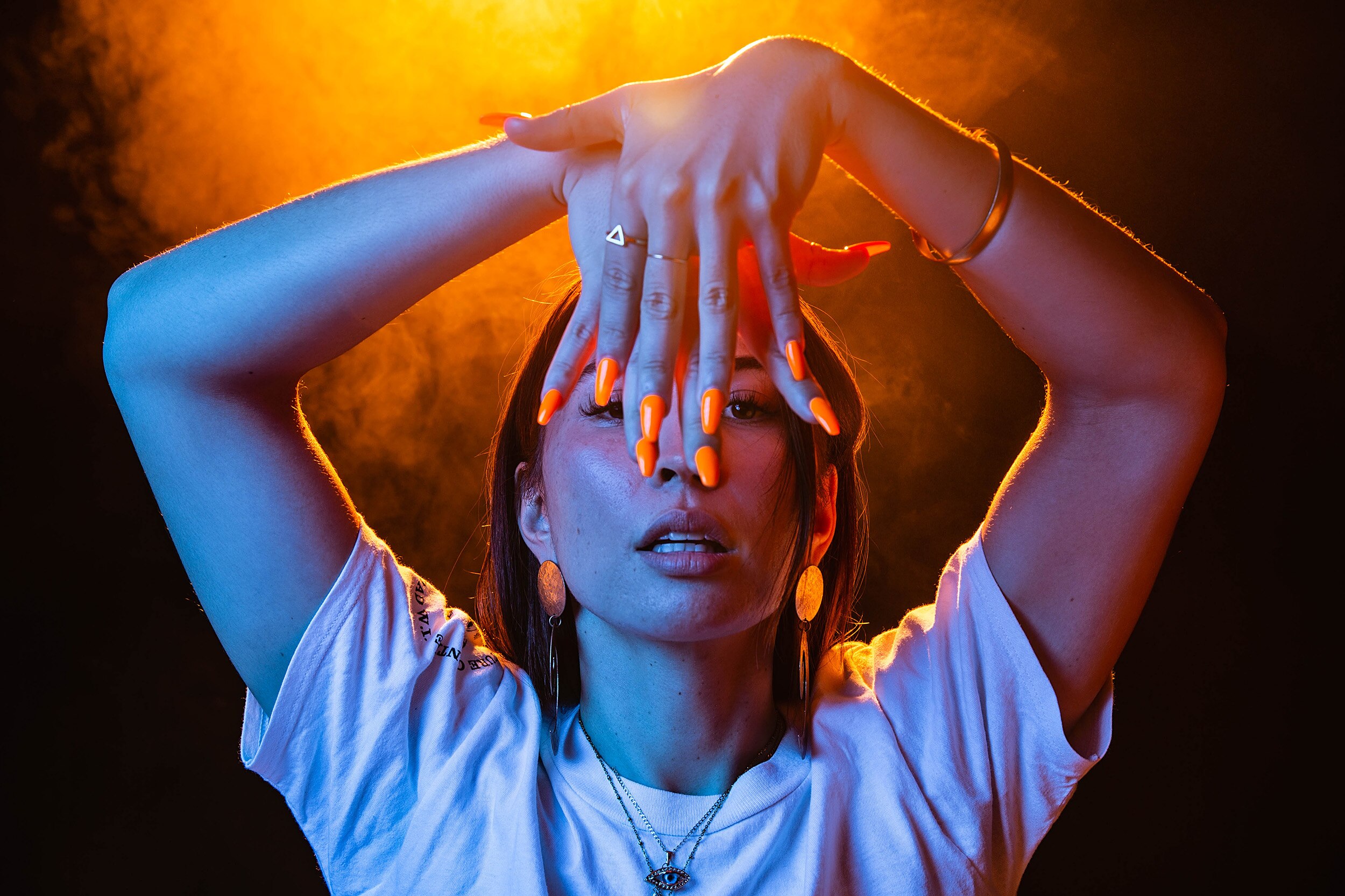 A dramatic colour portrait of Bhenji Ra holding above face and posing in front of dark background.