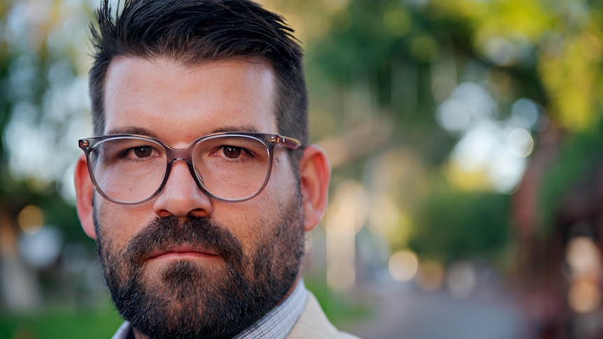 Close shot of man's face, with dark hair and beard and glasses. 