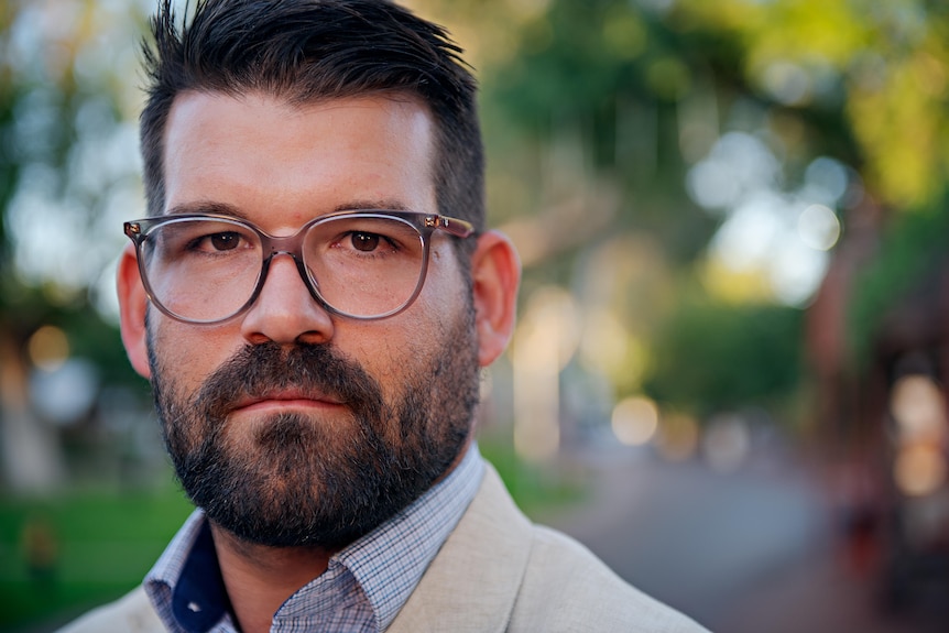 Close shot of man's face, with dark hair and beard and glasses. 