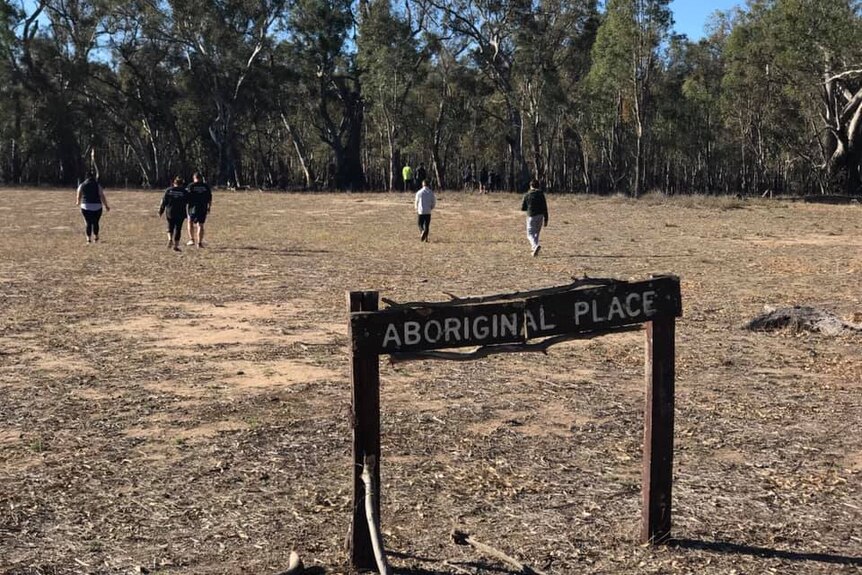 Children walk across a field past a sign that says 'Aboriginal place'