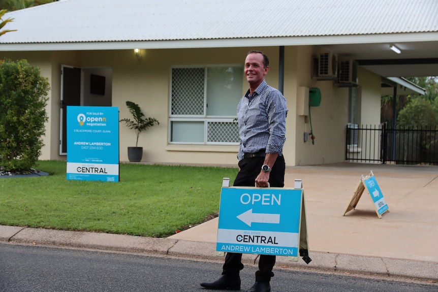 Real estate agent Andrew Lamberton holding an open for inspection sign in front of a house.