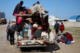  A group of people all loaded up into the back of a small truck with no back door.