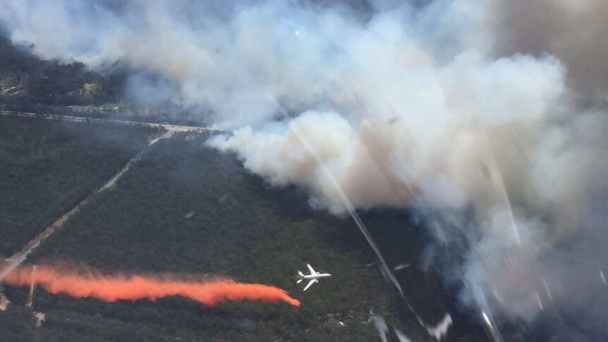 A plane drops orange fire retardant on a bushfire.