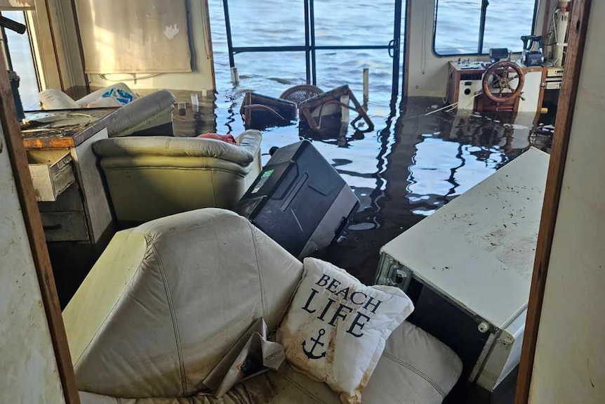 Inside the houseboat Bad Habits, inundated with water, with a couch floating in foreground