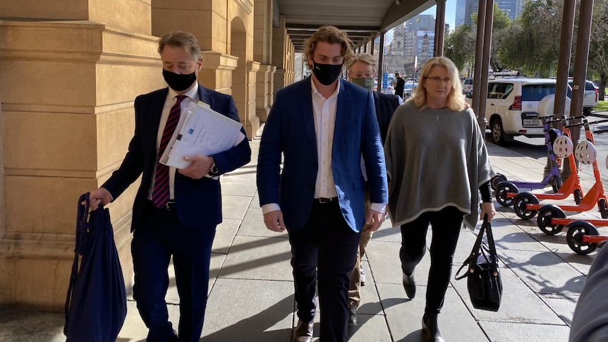 Two men in suits and a woman wearing a grey poncho walk outside court