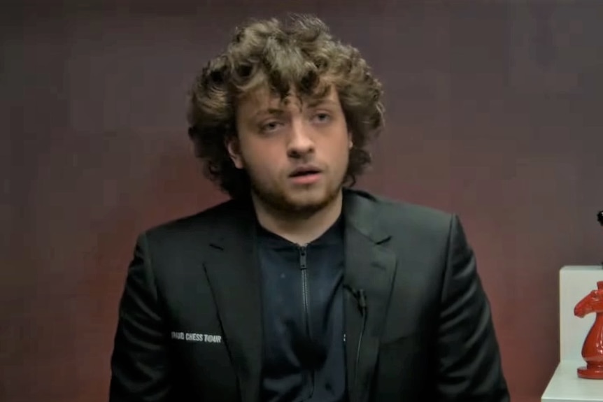 Screenshot of young man in a black jacket talking to camera in an interview