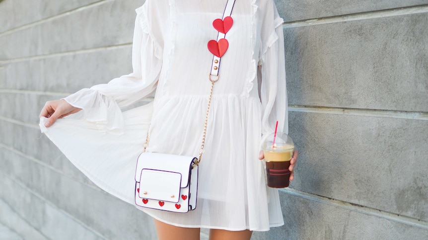 Woman in a white dress holds a coffee showing how vintage clothes can refresh your wardrobe for cheap.