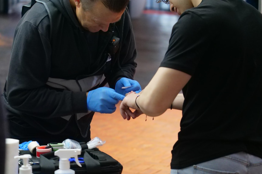 A man wearing blue gloves puts a band-aid on a young man's hand