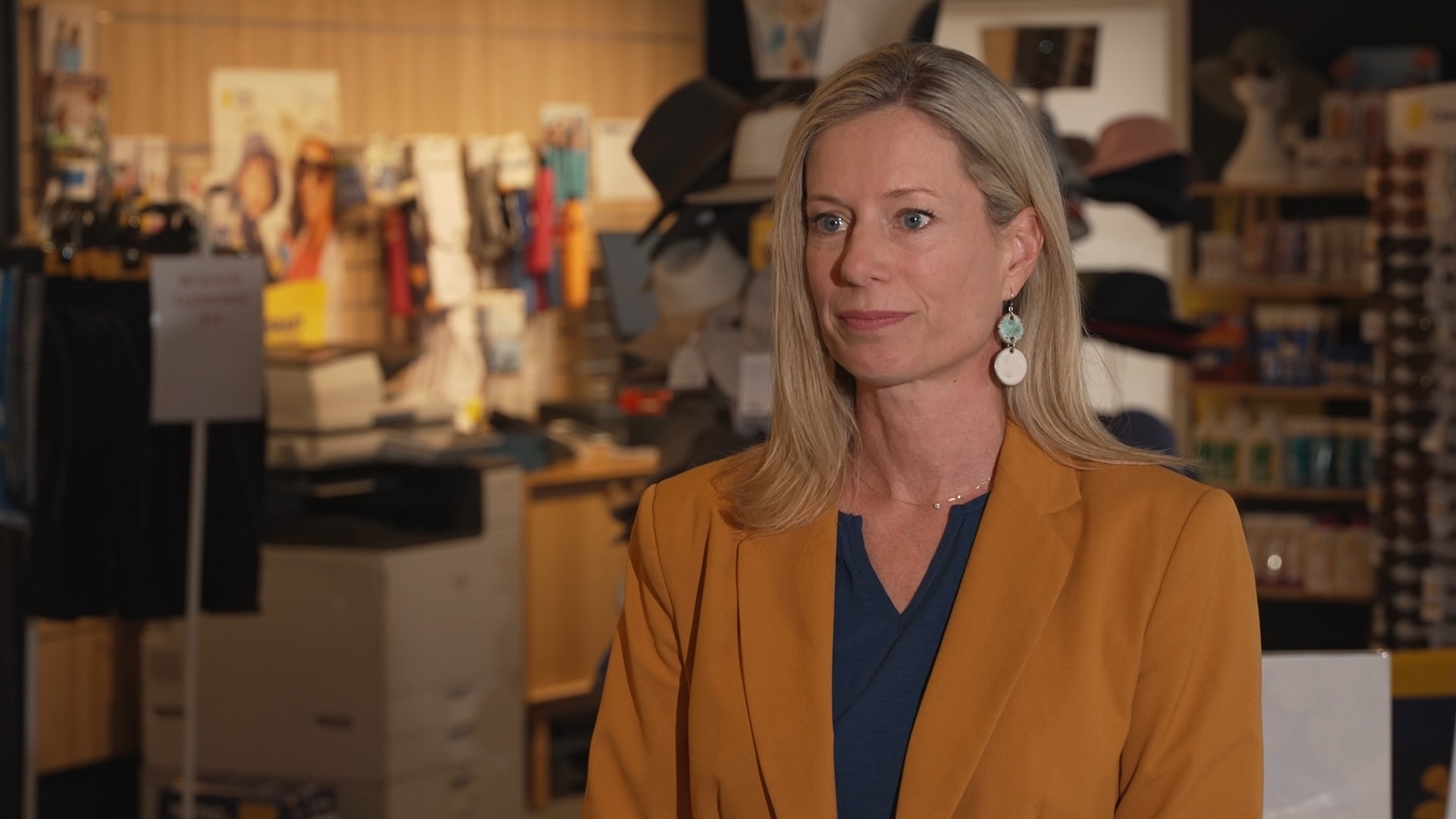 Rebecca White lleva un blazer color mostaza y tiene cabello rubio y aretes.