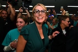 A woman wearing a teal shirt and black glasses smiles amid a sea of people. 