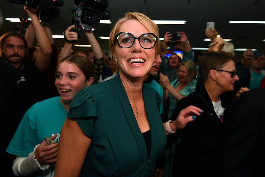 A woman wearing a teal shirt and black glasses smiles amid a sea of people. 