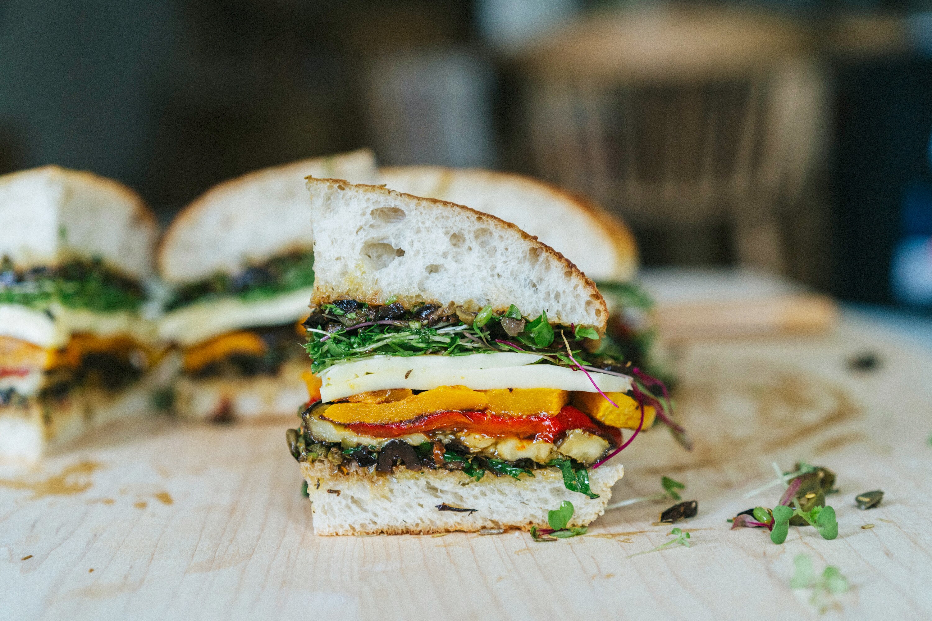 A sliced of layered roasted vegetable sandwich, filled with mozzarella, veggies and microgreens.