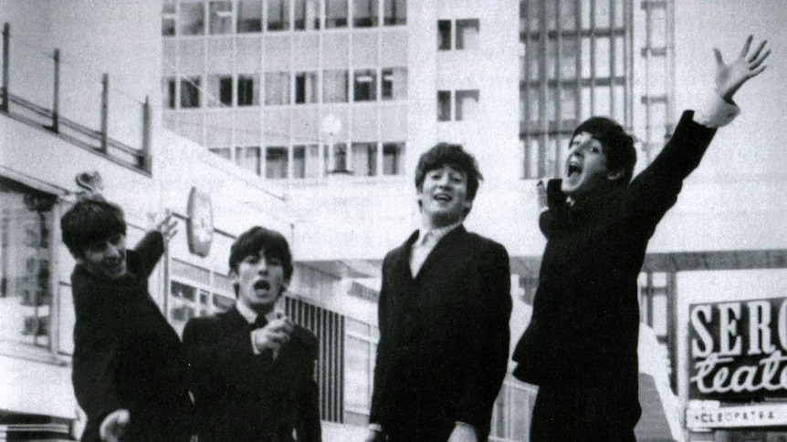 The Beatles in black suits and white shirts jumping in the air.