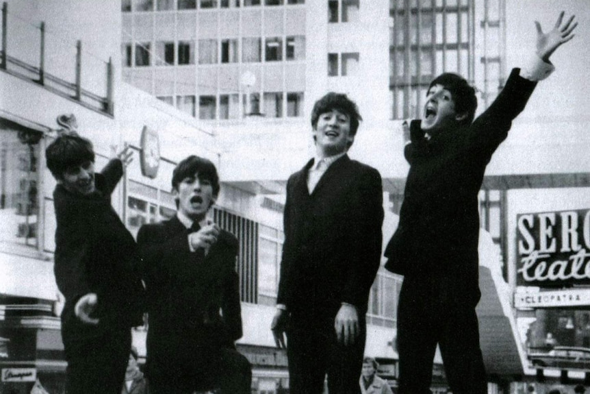 The Beatles in black suits and white shirts jumping in the air.