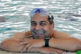 A middle-aged man wearing goggles smiles at the edge of a swimming pool