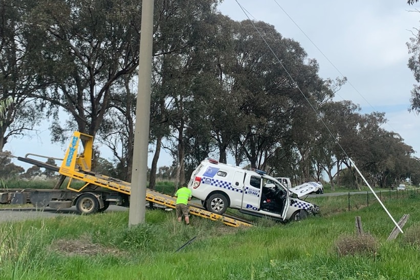 police vehicle being hauled on tow truck on regional road.