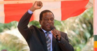 Emmerson Mnangagwa holds one arm up in the air as he speaks into a microphone.