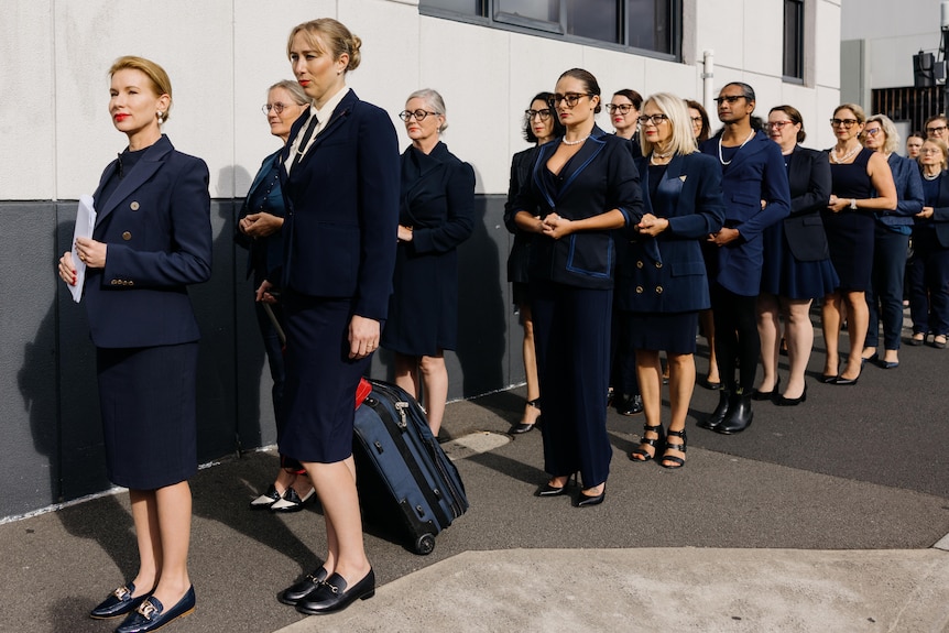 Women dressed in blue line up outside a building
