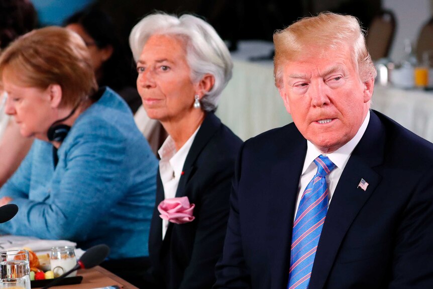 Trump looking grumpy, sitting next to  Lagarde and Merkel at summit.