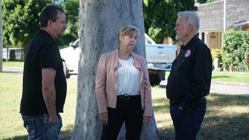 Two men in black shirts talk to each other with Sue Gilroy, middle, looking at one of them