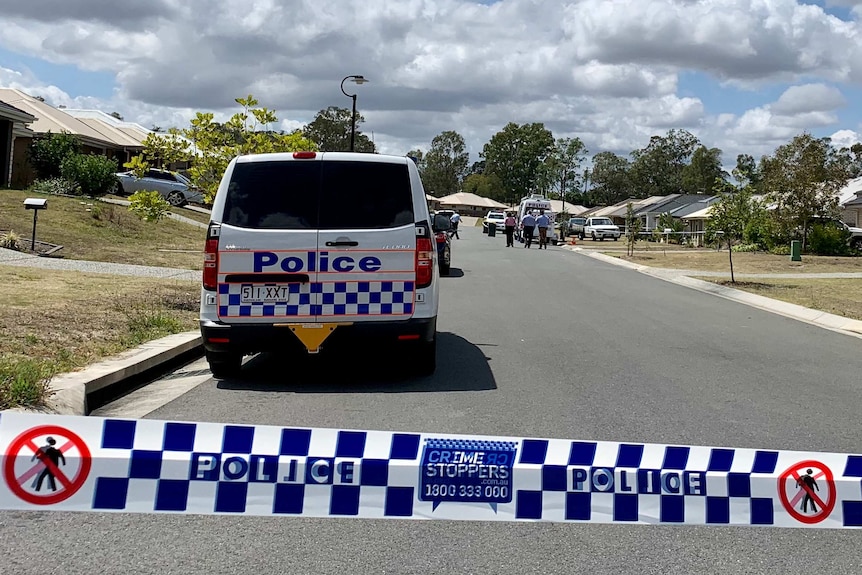 Crime scene tape blocks a suburban street containing police cars and detectives.