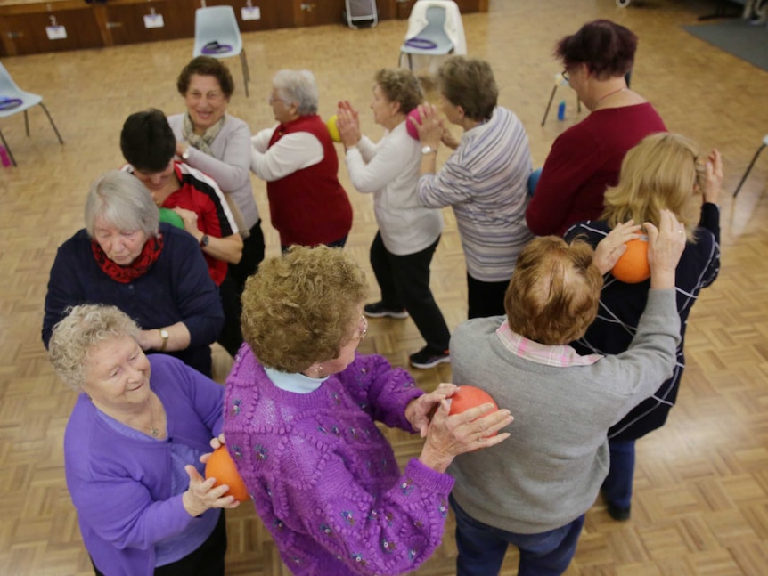 A group of elderly women standing in a circle holding up exercise balls to each others' backs. They're mostly smiling.