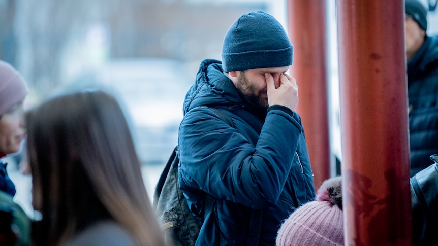 A man in a winter coat and beanie clutches his face to stem the flow of tears