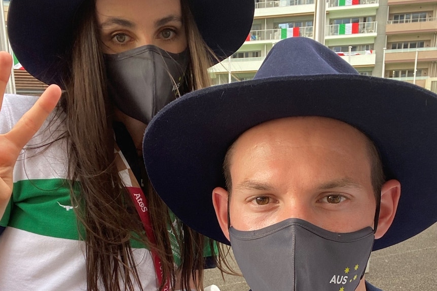 A man in a mask with a woman in a mask behind him doing a peace sign.