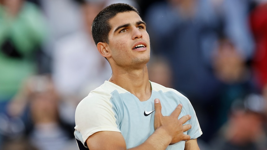 A young man stands looking up at the grandstands with his hand on his heart after a French Open match. 