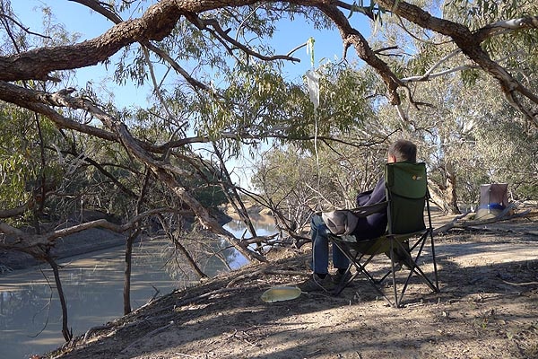 A man sits on a camping chair by a riverbed