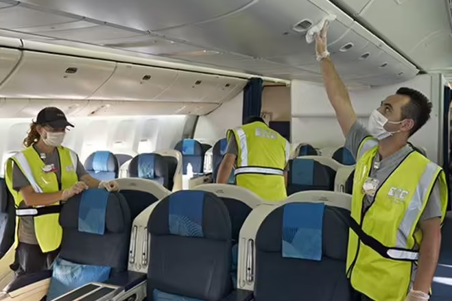 Three people in high viz vests clean the cabin of an aircraft