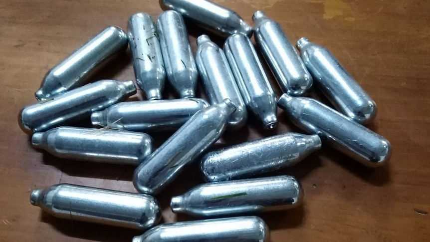 More than a dozen small silver canisters on a wooden table