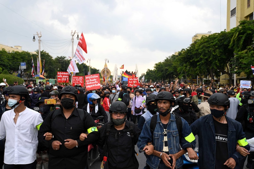 Five men in black helmets and masks in front of a large group of people.