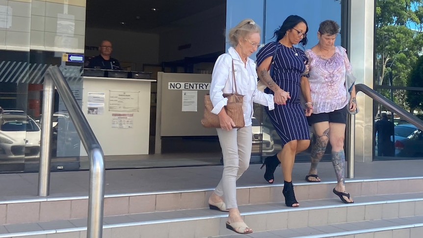 Woman with dark hair in dark blue dress with thin stripes leaves court with two other women