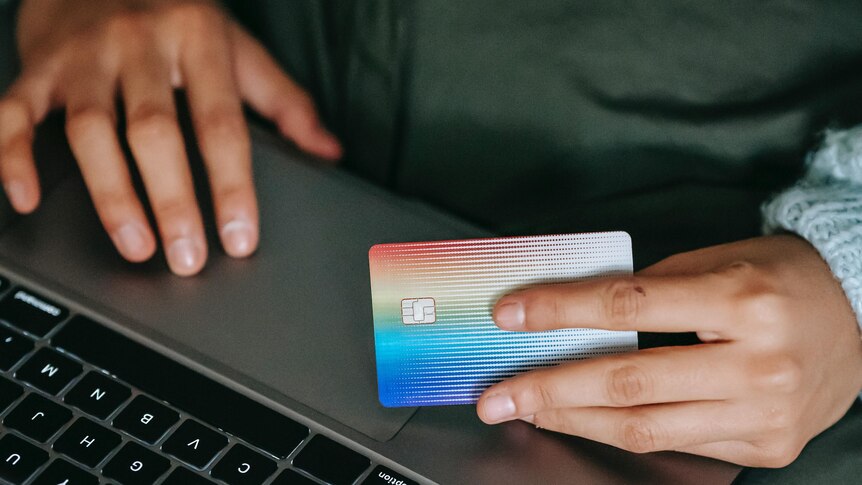 One hand on a laptop's trackpad while another hand holds a credit card
