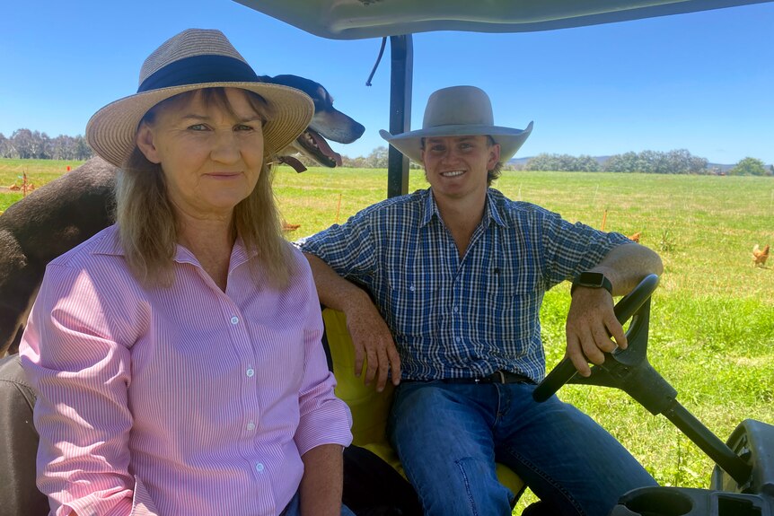 A woman and a younger man smile while sitting in a golf buggy on a farm.