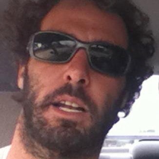 A tight head shot of Alejandro Travaglini wearing a white shirt and sunglasses.