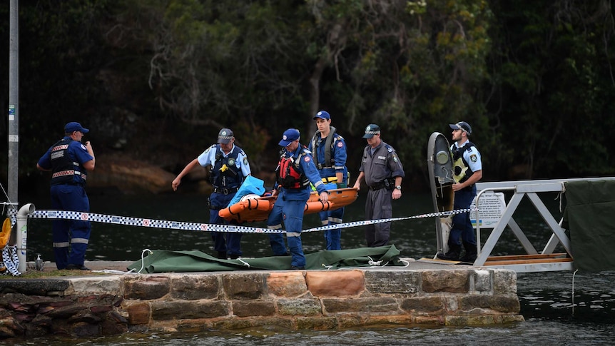 The body of a seaplane passenger is covered in a blue sheet and carried on a stretcher by four police officers.