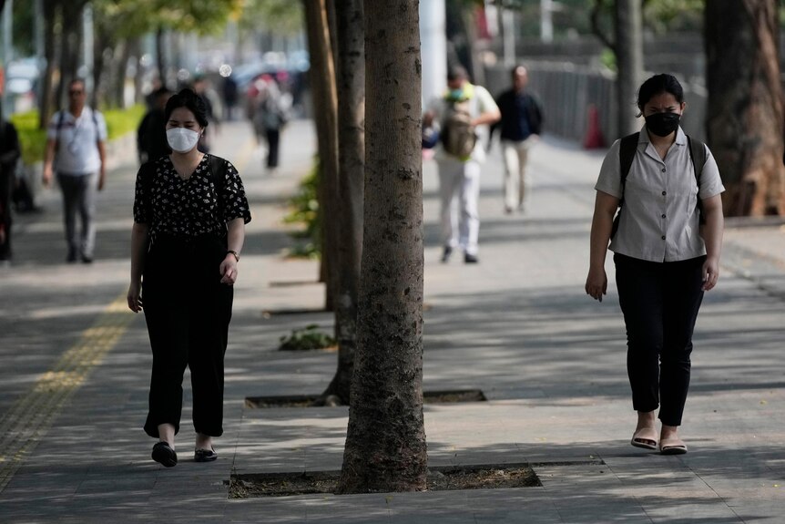 Two women walking down a street in Jakarta wearing masks.