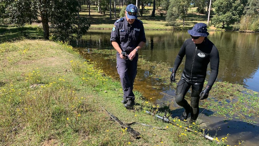 A police officer and diver examine a firearm discovered in a dam near Taree