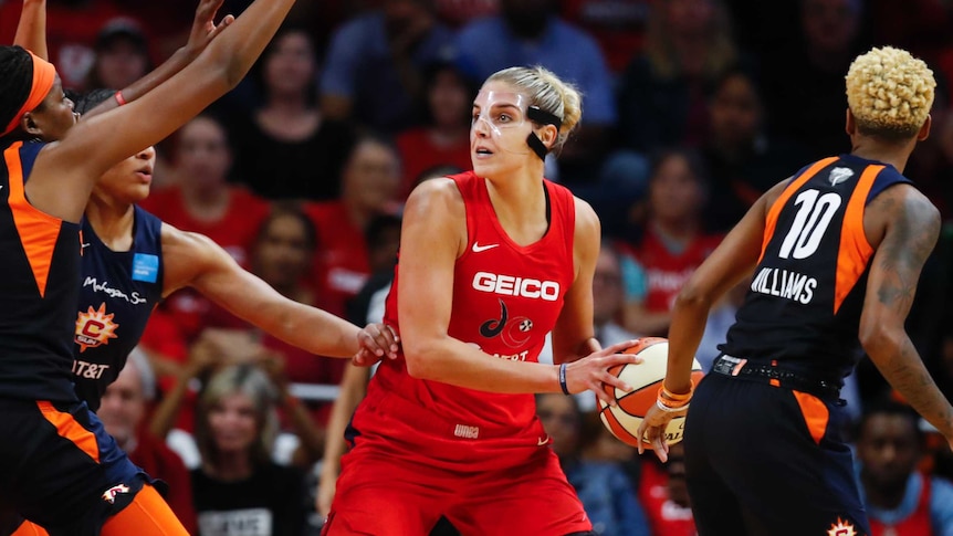 Washington Mystics player Elena Delle Donne, wearing a clear face mask, holds the basketball as she is guard by Connecticut Suns