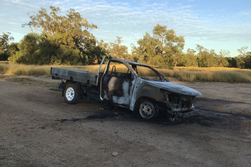A burnt out ute on a remote dirt road.