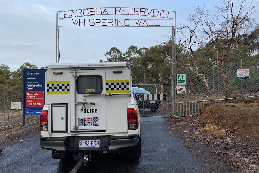 A police car blocks the road in front of a closed gate with a sign that reads 'Barossa Reservoir Whispering Wall'