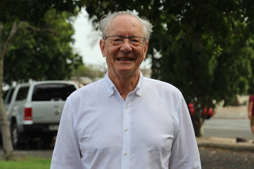 A man wearing a white shirt and glasses smiles at the camera