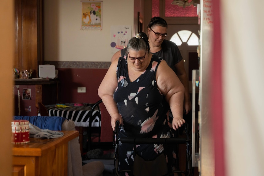 Younger woman helps older woman use a walker to get through a crowded room 