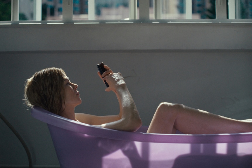 A TV still of Nicole Kidman lying in a pink bath looking at her phone.