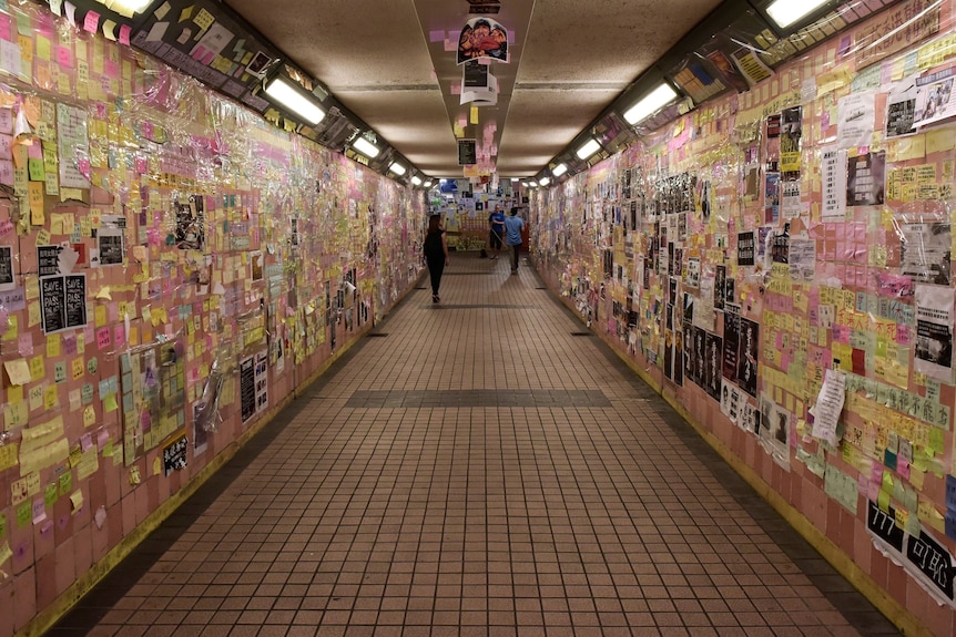 An underground walkway with banners, posters and sticky notes all over the walls