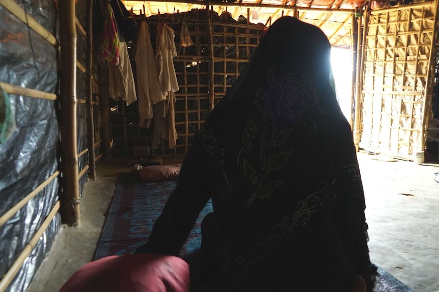 Noor sits gingerly on the floor of a friend's hut.