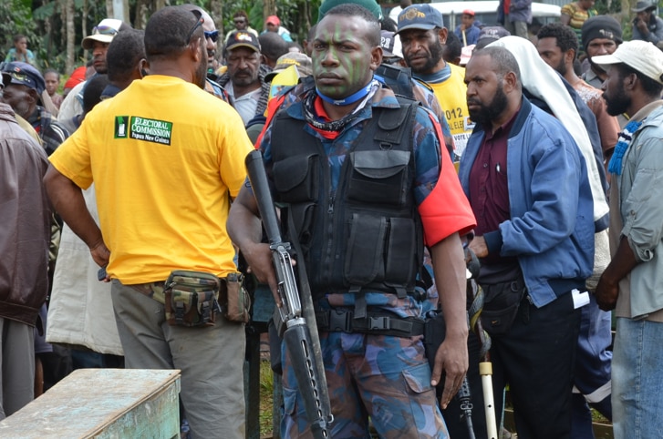 An armed guard watches over voters lining up to cast their ballots in Tari, PNG.