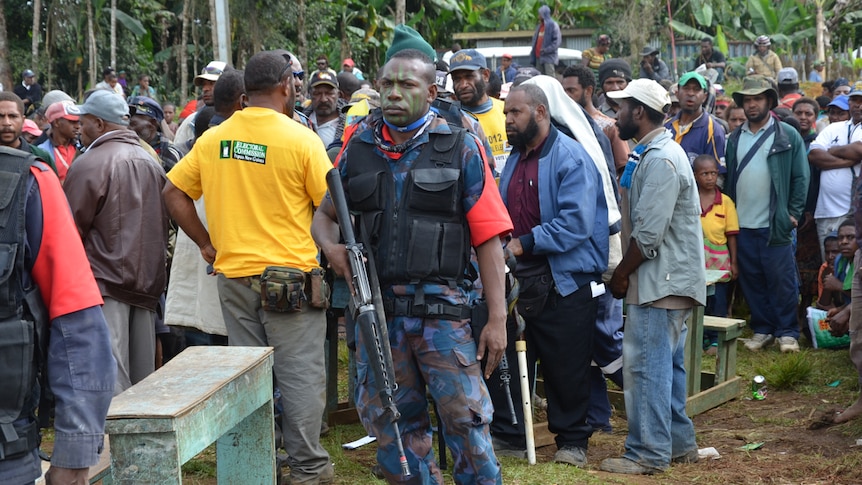 An armed guard watches over voters lining up to cast their ballots in Tari, PNG.